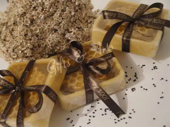 Sabonetes artesanais de Favo de Mel com quadrados com formato de colmeia decolados com laços pretos com inscrições douradas, ao lado um favo de mel.
