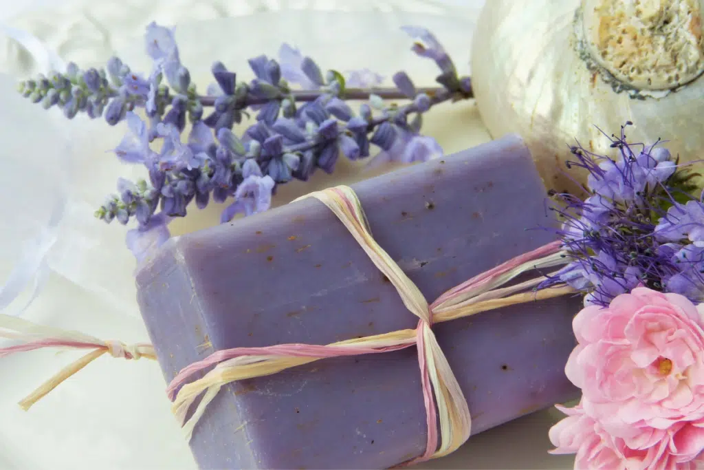sabonete artesanal de lavanda decorado com elásticos coloridos e folhas de lavanda ao lado.