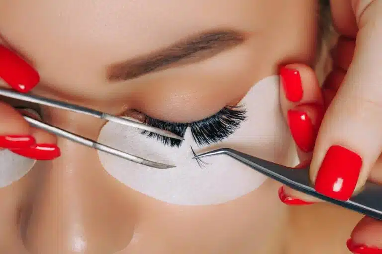 Lash Designer : Seja uma projetista de cílios de sucesso Mãos de uma profissional de lash designer segurando pinças para colocar fios de sobrancelhas numa cliente de pele morena.