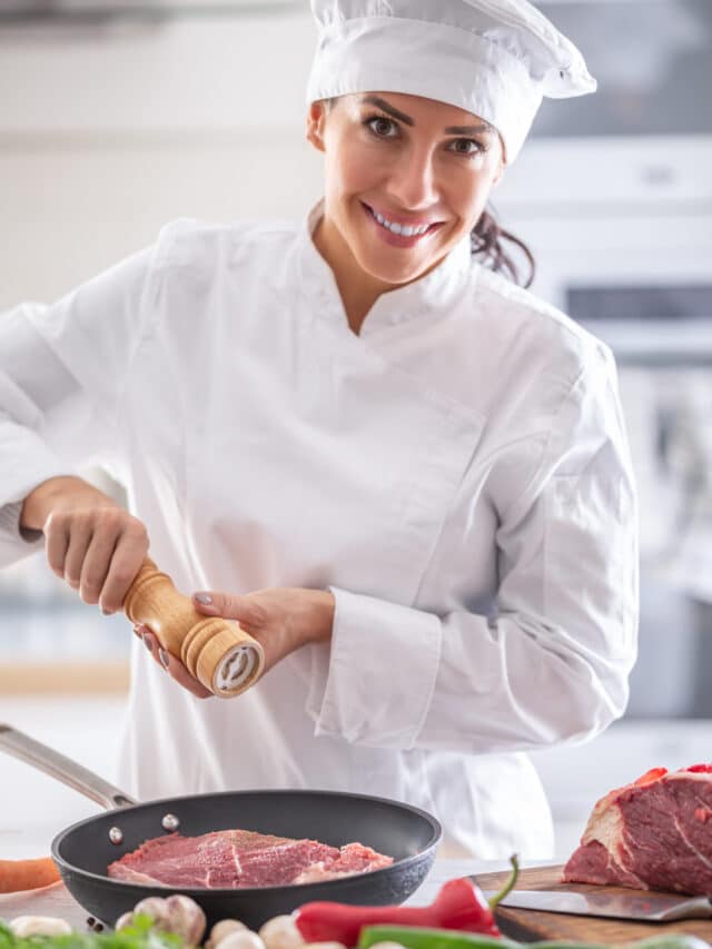 Profession of chef shown through a female in rondor peppering steak in a pan.
